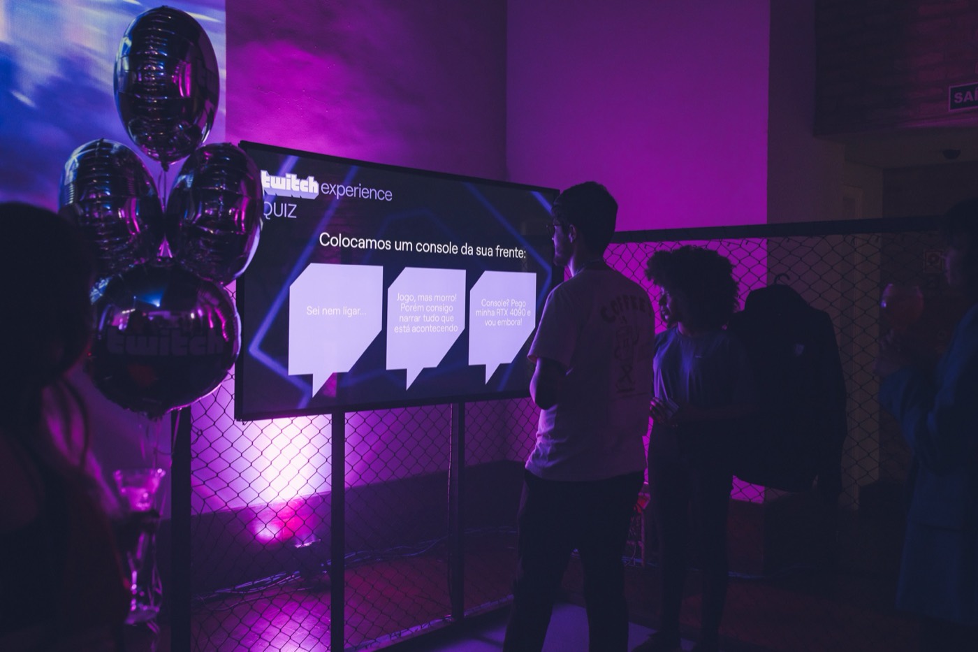 Participants in front of a "twitch experience" quiz screen with metallic balloons and purple light