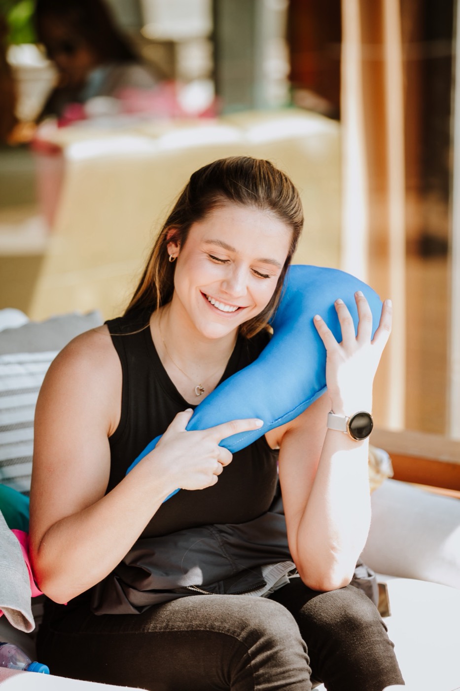 Seated person smiles with eyes closed, resting their face against an elongated blue cushion