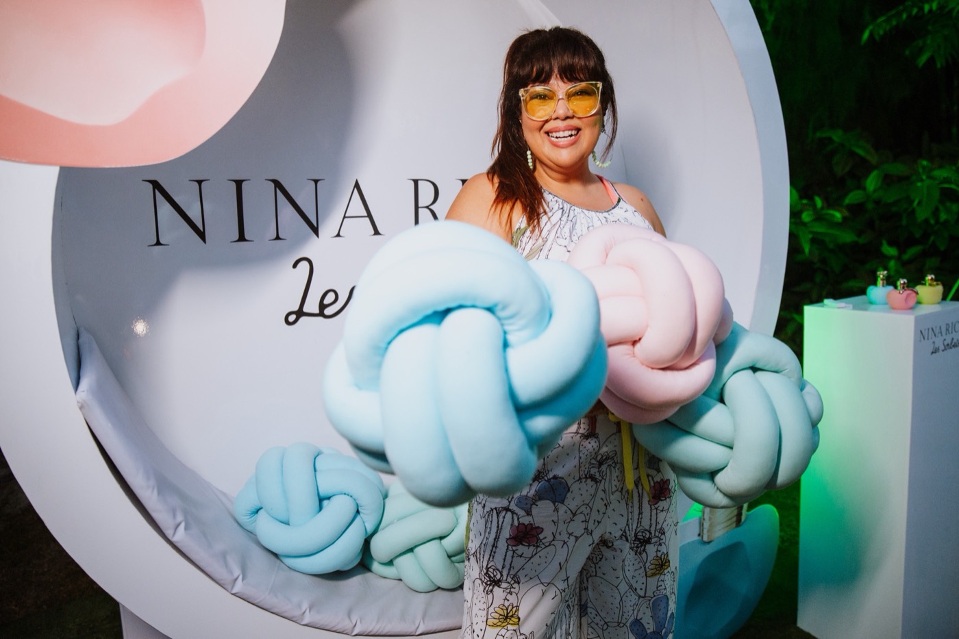 Person in yellow glasses smiles in front of a white circular panel decorated with pastel knot cushions