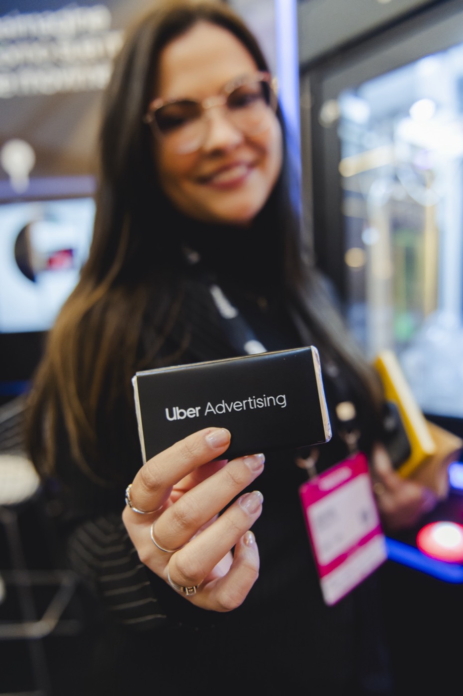 Smiling person, out of focus, holds toward the camera a bar in black wrapping reading "Uber Advertising"