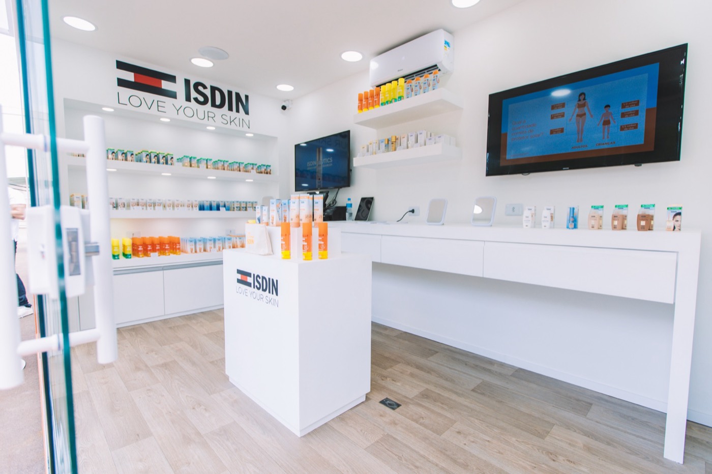 White store interior with a counter, product shelves, two wall screens and the "ISDIN LOVE YOUR SKIN" logo