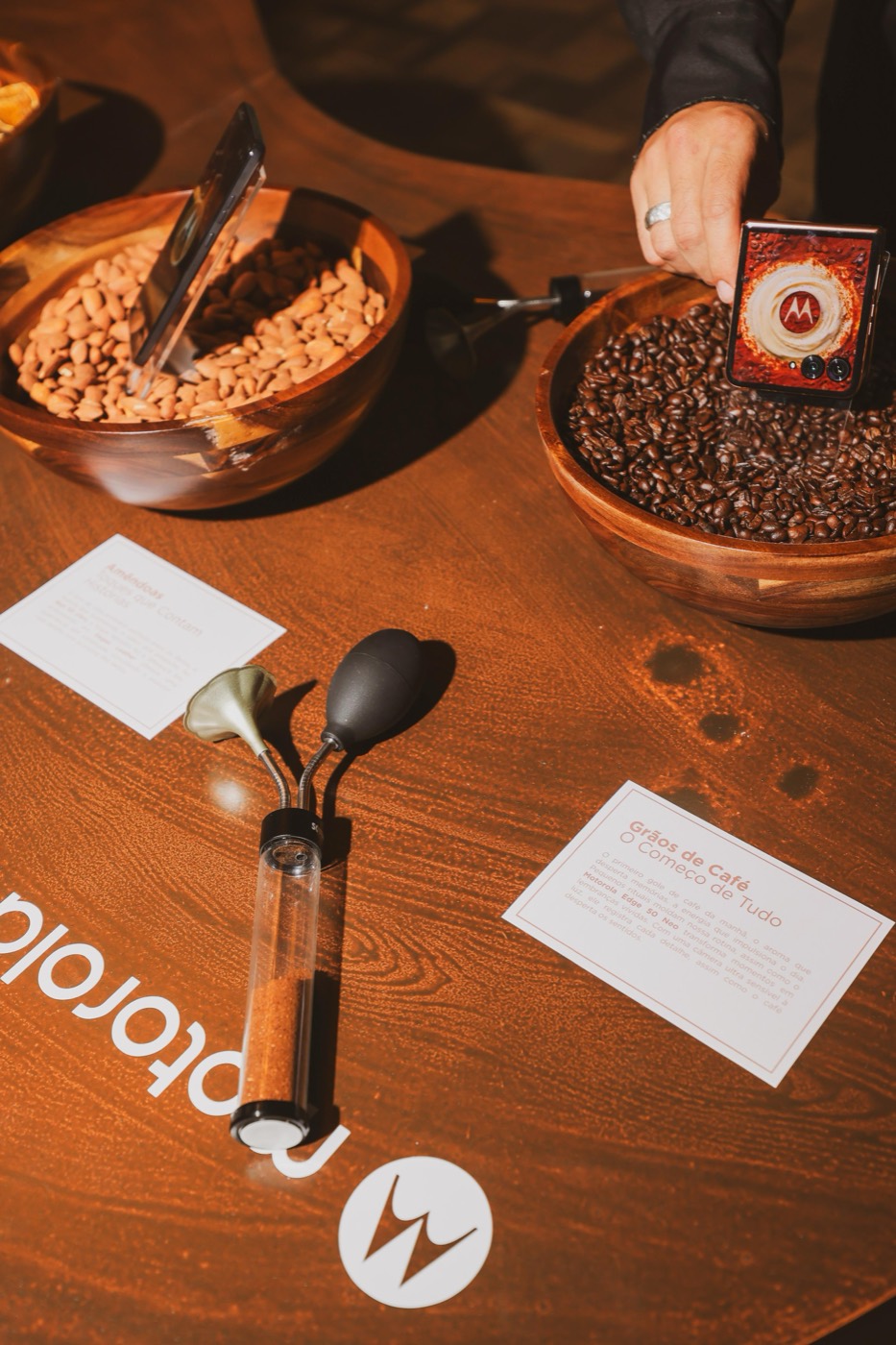 Wooden table with bowls of coffee beans, explanatory cards and a hand holding a flip phone, with the "motorola" logo