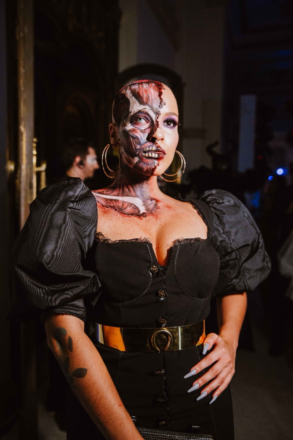 Person with half their face made up as a skull poses in black clothing with puffed sleeves
