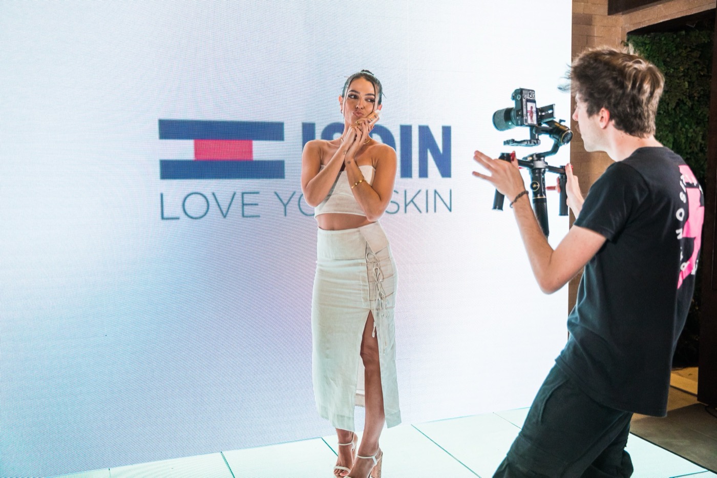 Person poses in front of an LED wall with the "ISDIN" brand while another films them with a gimbal camera