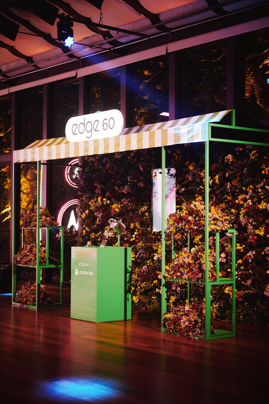 Booth with striped awning, green frame and flower wall, with an "edge 60" sign and a "motorola" pedestal