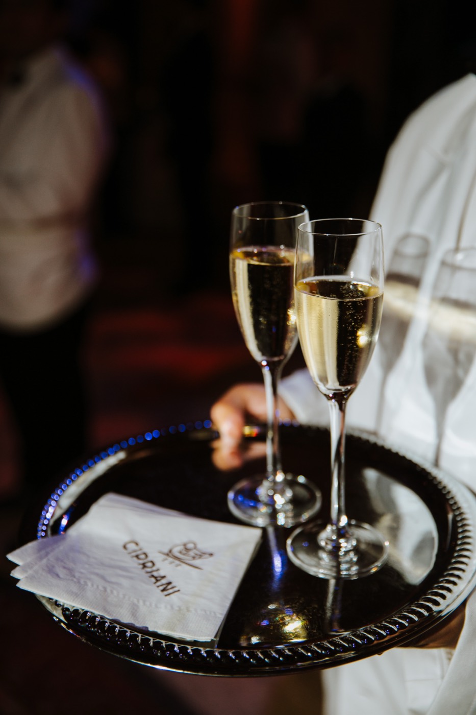 Silver tray with two flutes of sparkling wine and napkins, carried by a person in a white jacket