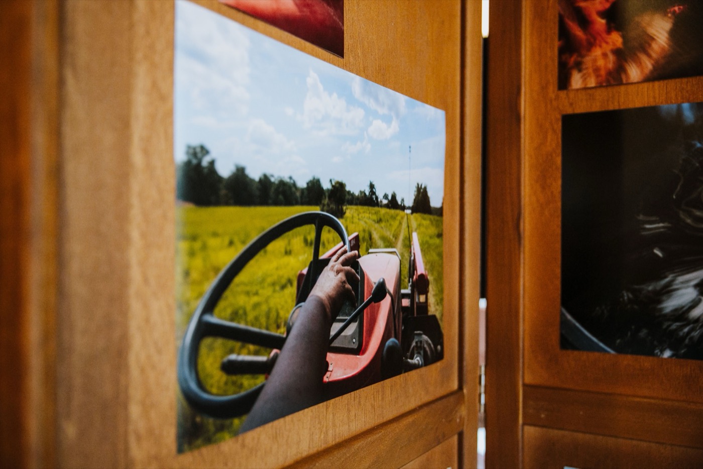 Wooden panel with a printed photo of hands on a tractor steering wheel facing a field