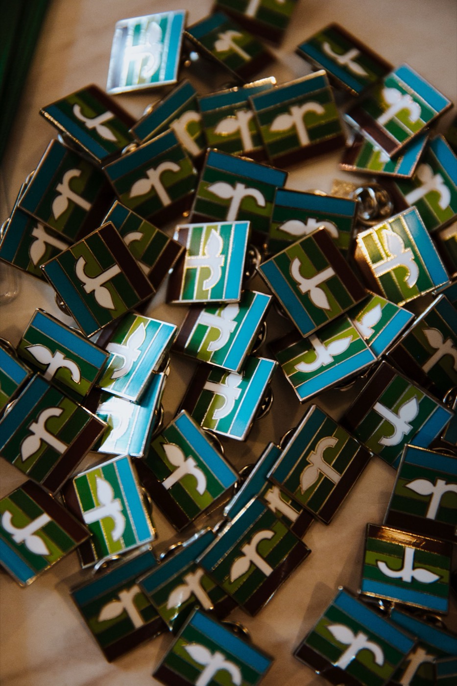 Pile of square enamel pins with a white sprout design over green and blue stripes