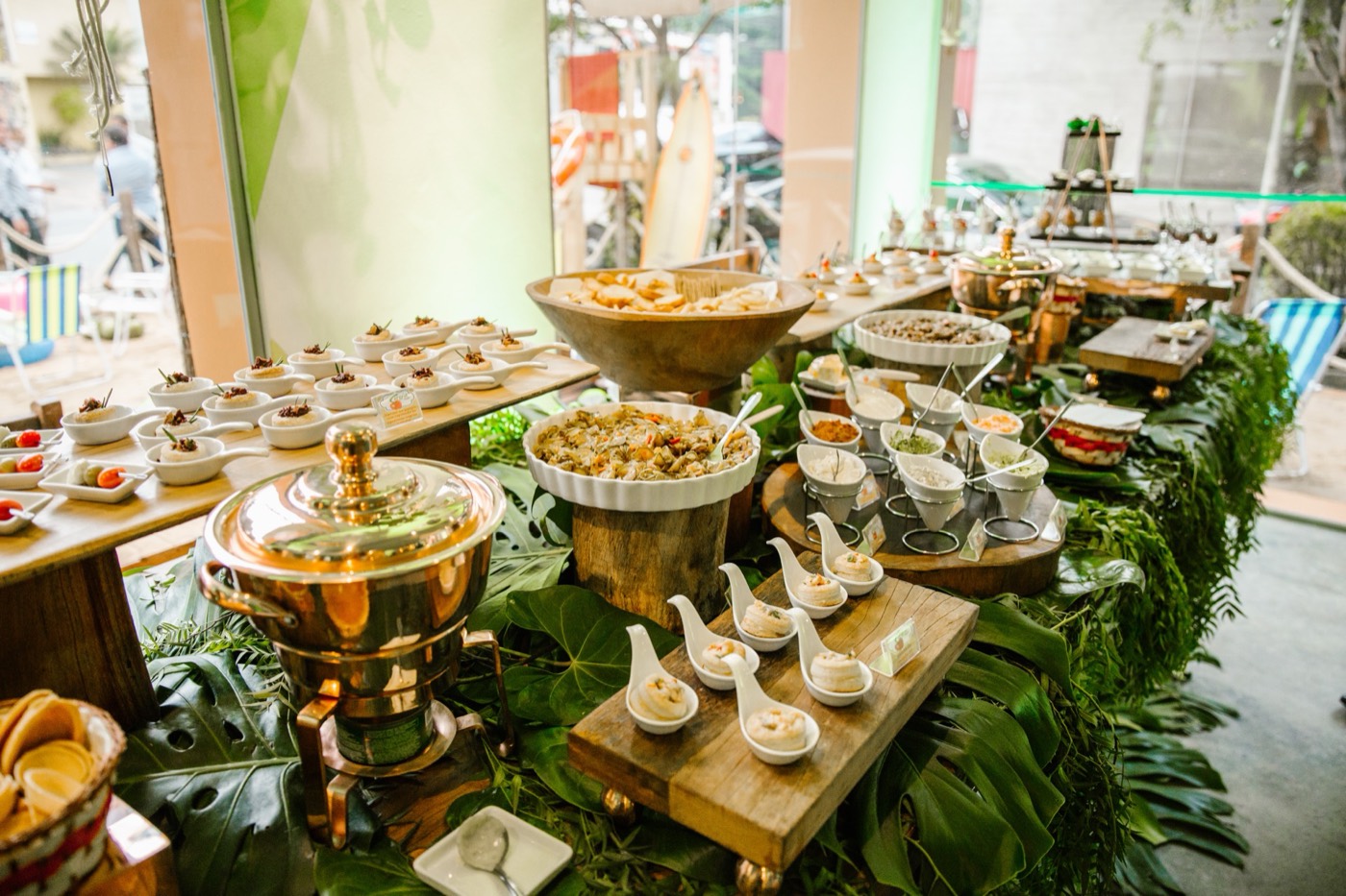 Buffet table decorated with foliage, with a copper chafing dish, salads and individual portions in cups and spoons