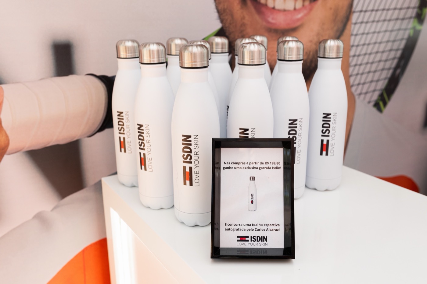 White insulated bottles with the "ISDIN" brand lined up on a counter beside a small framed notice
