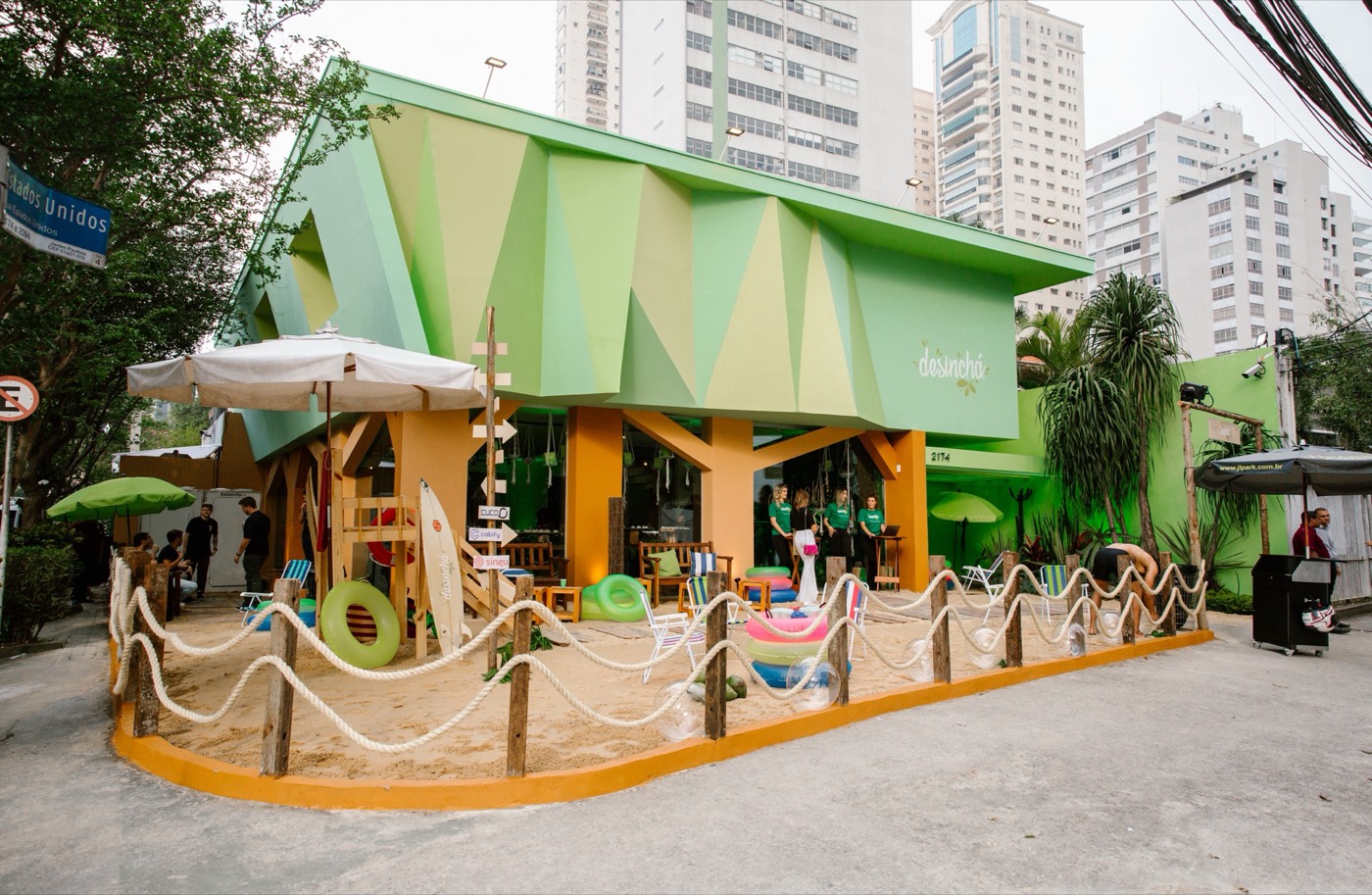 Geometric green facade of a house with a rope-fenced sand area, a parasol and inflatable pool floats