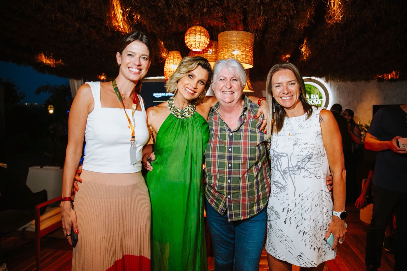 Four people pose arm in arm at night under a thatched roof with wicker lamps