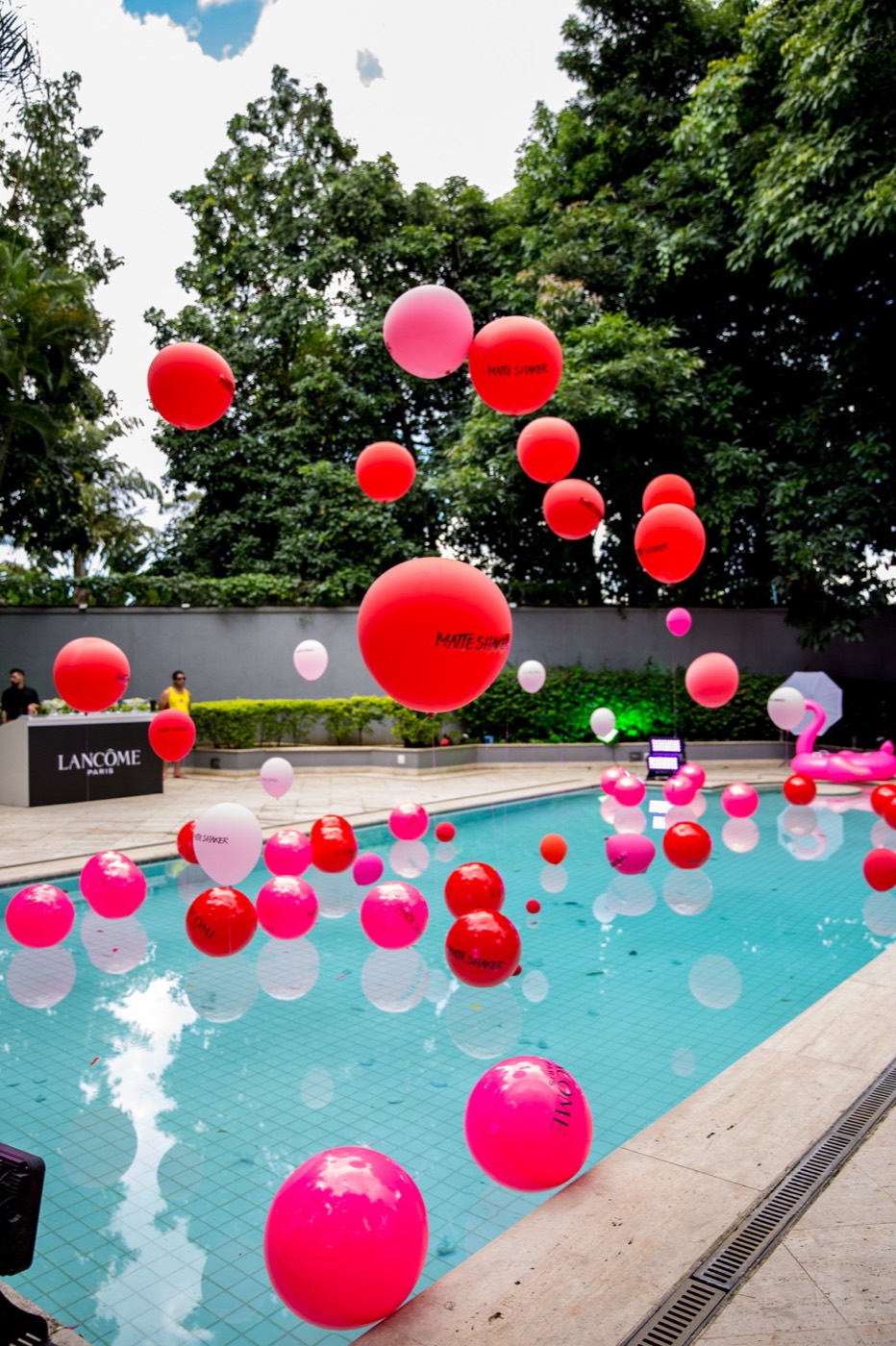 Pool with red and pink balloons floating and suspended in the air, with a "LANCÔME PARIS" counter in the background