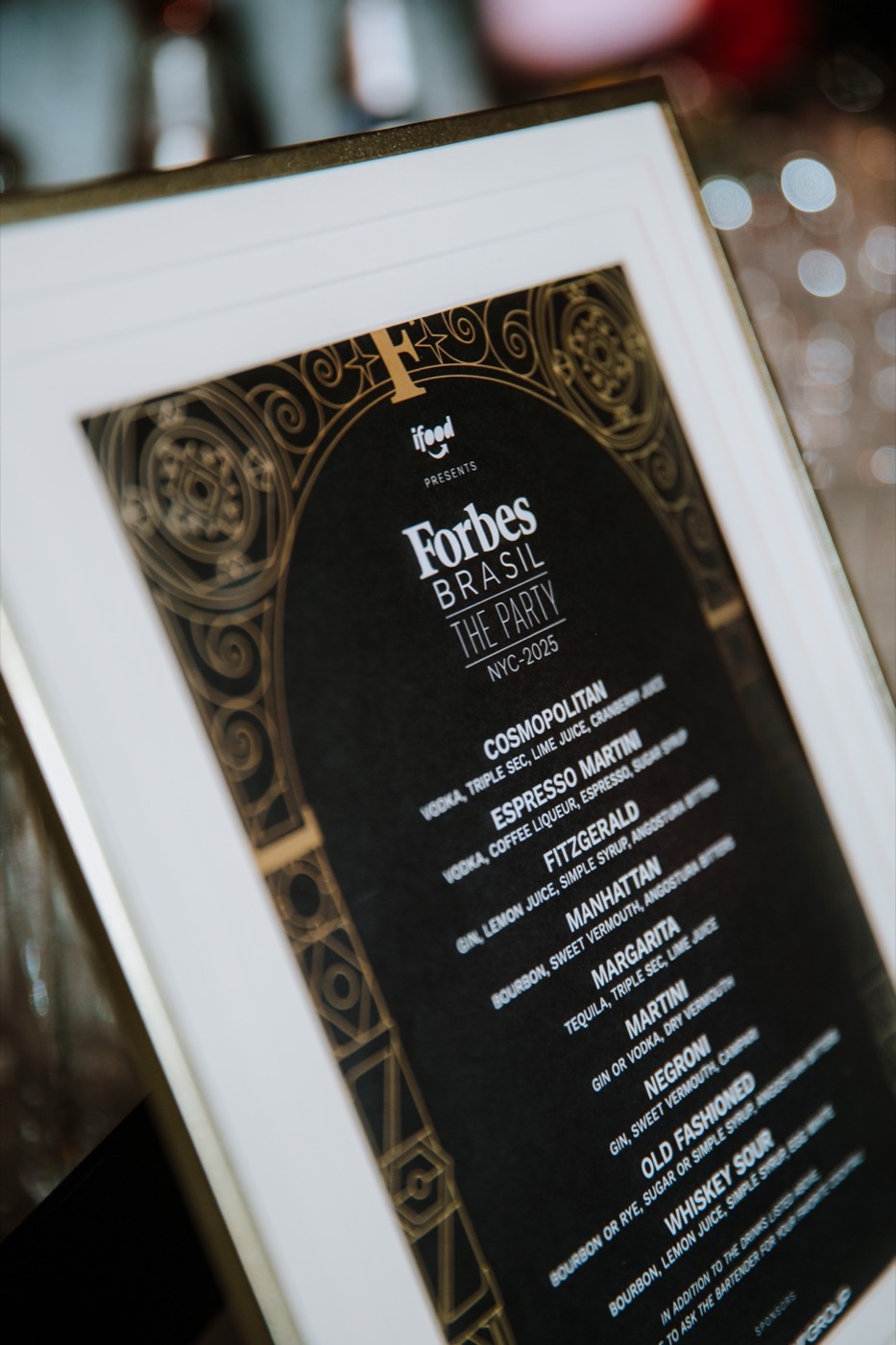 Close-up of a framed cocktail menu, with a gold frame and the title "Forbes BRASIL THE PARTY"