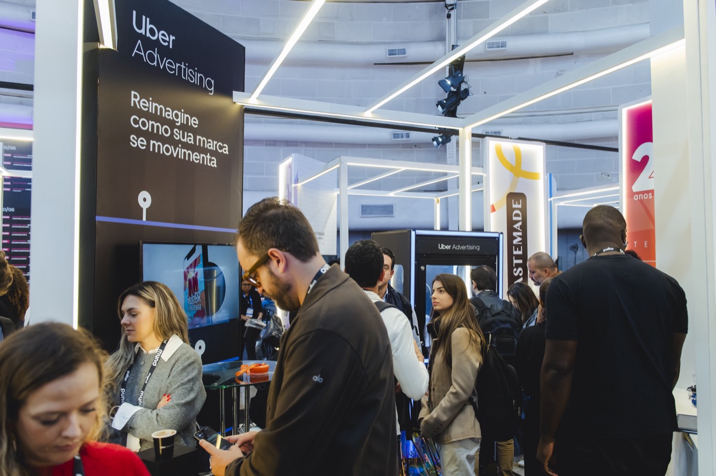 Attendees with badges move through a booth with an "Uber Advertising" panel and white light frames