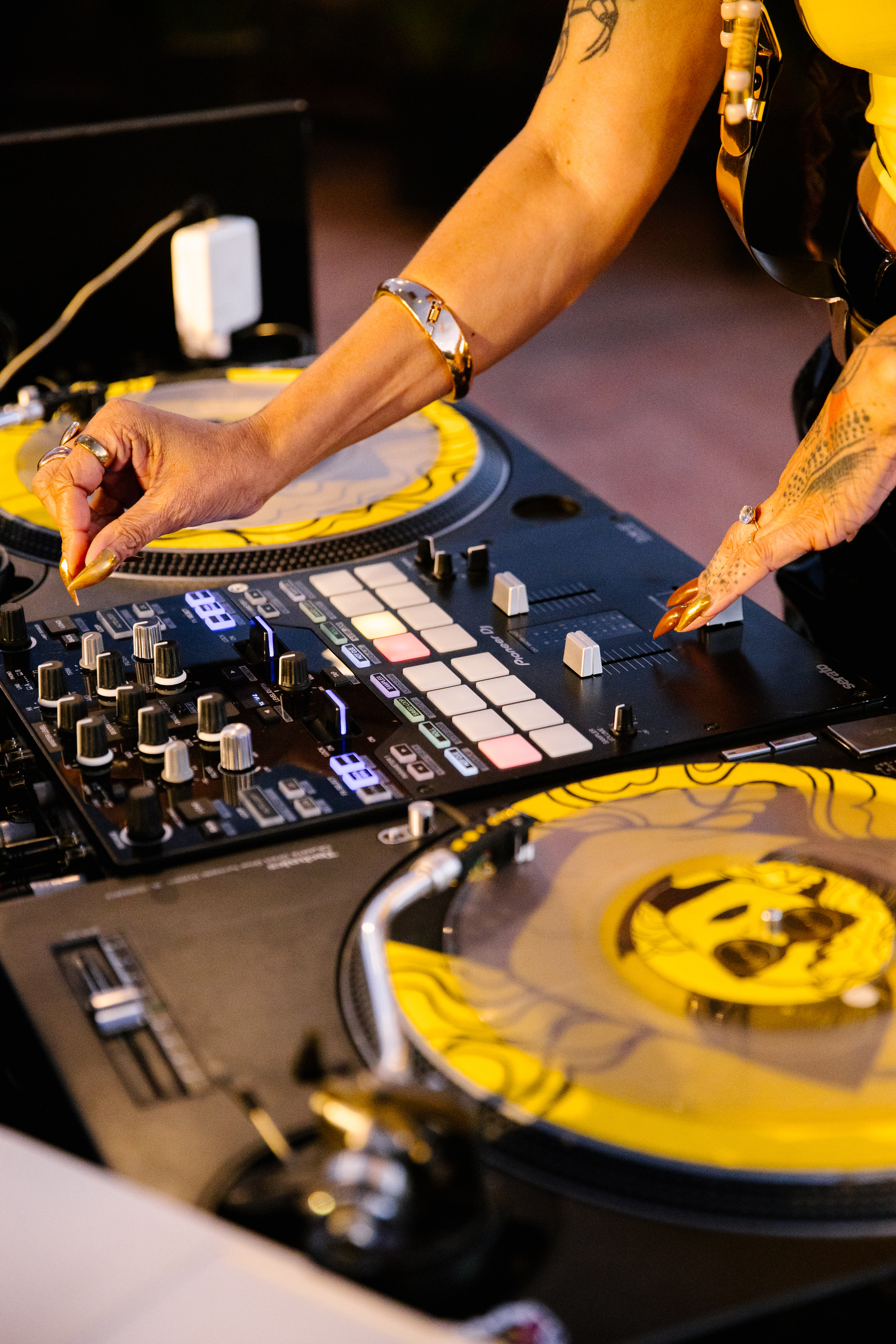 DJ's hands adjust turntables and a mixer with yellow details