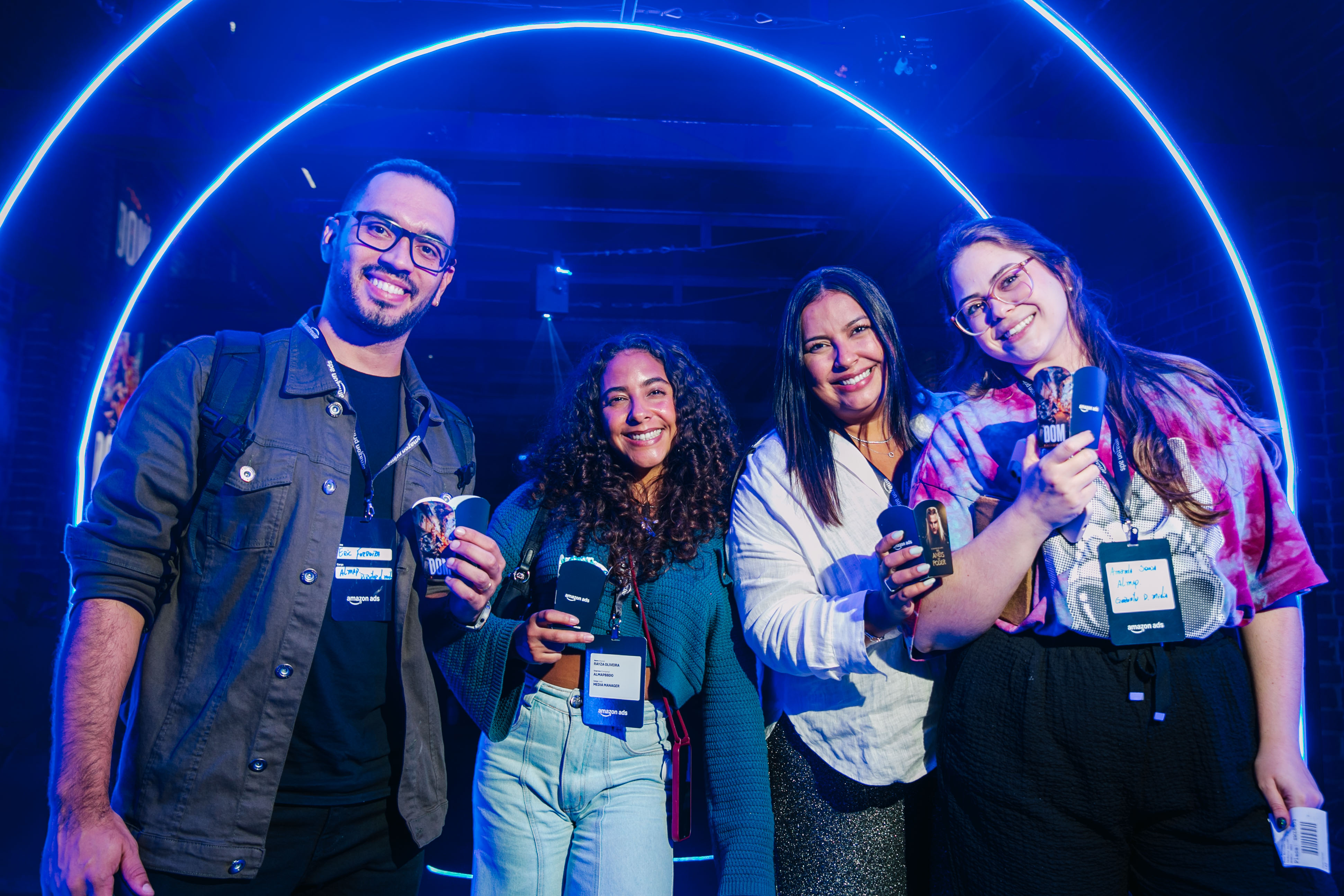 Four people wearing badges smile at the camera under blue neon light arches